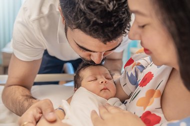 Closeup of father kissing his newborn baby's head, while mother holds baby in her arms.