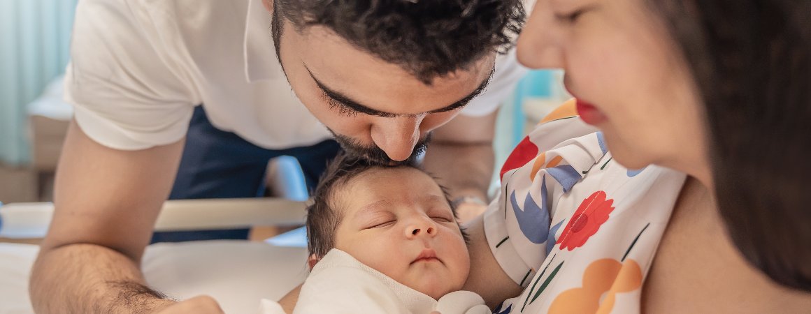 Closeup of father kissing his newborn baby's head, while mother holds baby in her arms.